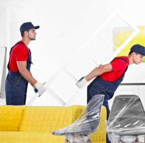 Umzug in Grevenbroich Zwei Helfer tragen ein Möbelstück an einem gelben Sofa vorbei – Umzug in Grevenbroich