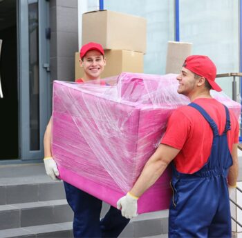Umzug in Grevenbroich Zwei Umzugshelfer tragen ein in Folie gepacktes Möbelstück – Umzug in Grevenbroich