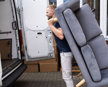 Möbellift Grevenbroich: Helfer tragen ein graues Sofa aus einem Transporter